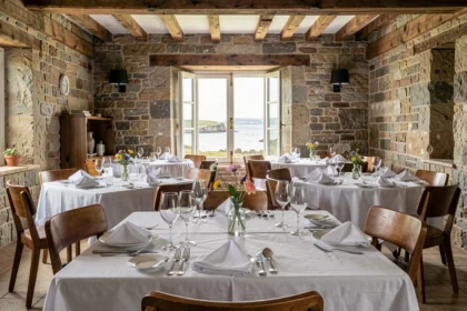 Salle de restaurant gastronomique breton avec murs en pierre, tables dressées avec élégance et vue sur la côte bretonne